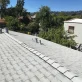 A gray shingle roof with three vents and ridge caps under a clear blue sky, overlooking distant houses and trees.